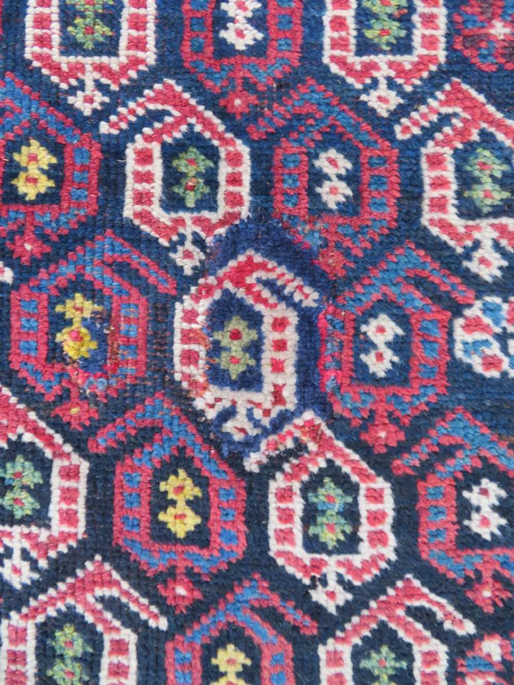 An antique hand-knotted Kurdish Kelleh long rug featuring a navy blue central field filled with repeating geometric motifs within multi-coloured yellow and red borders. View X