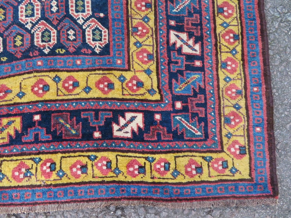 An antique hand-knotted Kurdish Kelleh long rug featuring a navy blue central field filled with repeating geometric motifs within multi-coloured yellow and red borders. View XII