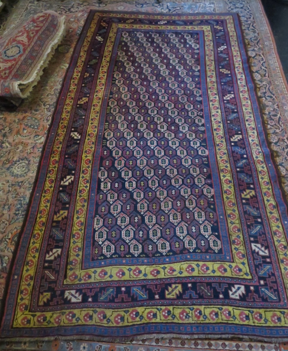 An antique hand-knotted Kurdish Kelleh long rug featuring a navy blue central field filled with repeating geometric motifs within multi-coloured yellow and red borders. View XVII