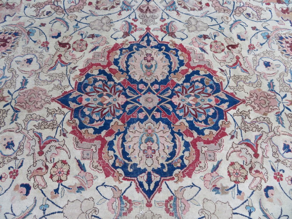 A large hand-knotted Persian Tabriz carpet featuring a central navy blue and red medallion on a cream field with floral vines and a prominent red border. View VI