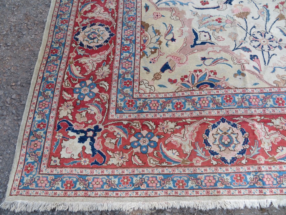 A large hand-knotted Persian Tabriz carpet featuring a central navy blue and red medallion on a cream field with floral vines and a prominent red border. View X