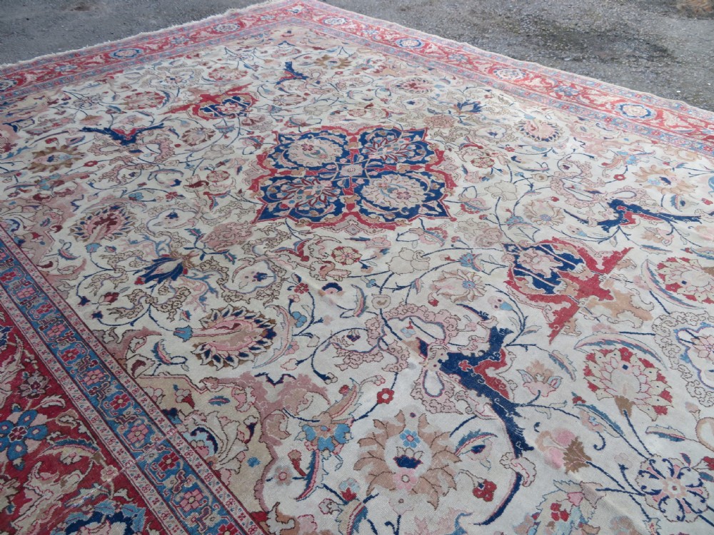 A large hand-knotted Persian Tabriz carpet featuring a central navy blue and red medallion on a cream field with floral vines and a prominent red border. View XII