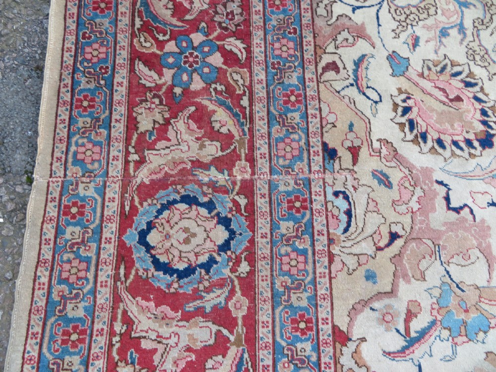 A large hand-knotted Persian Tabriz carpet featuring a central navy blue and red medallion on a cream field with floral vines and a prominent red border. View XV