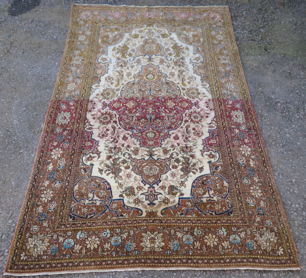 An antique hand-knotted Isfahan wool rug featuring a red central floral medallion on an ivory field surrounded by terracotta and blue floral borders.