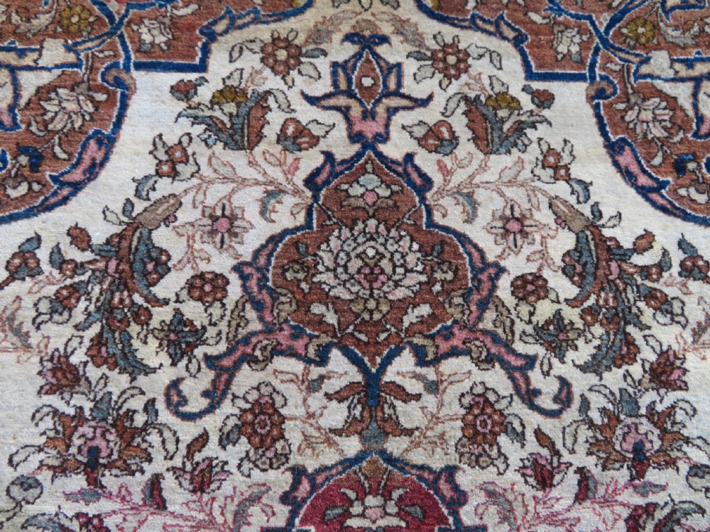 An antique hand-knotted Isfahan wool rug featuring a red central floral medallion on an ivory field surrounded by terracotta and blue floral borders. View V