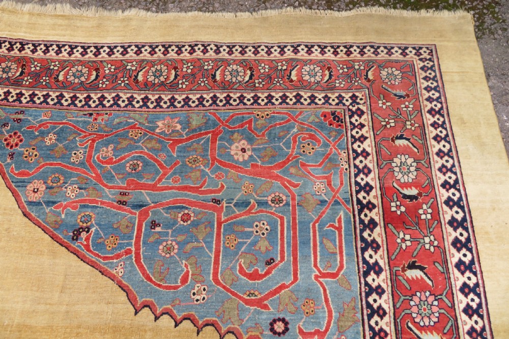 A large hand-knotted antique Persian Bidjar carpet featuring a gold yellow field, central diamond medallion, blue corner spandrels, and a patterned red border. View XV
