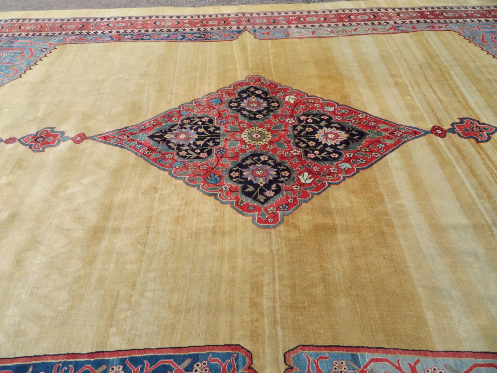A large hand-knotted antique Persian Bidjar carpet featuring a gold yellow field, central diamond medallion, blue corner spandrels, and a patterned red border. View XXV