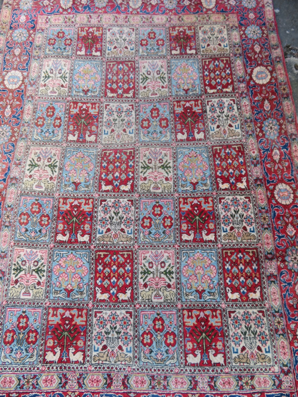 A hand-knotted Persian Qum rug featuring a grid tile pattern filled with floral and animal motifs inside a detailed red border. View IV