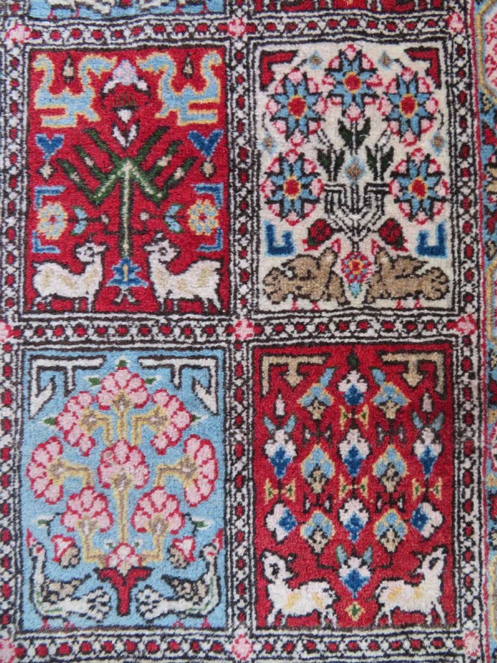 A hand-knotted Persian Qum rug featuring a grid tile pattern filled with floral and animal motifs inside a detailed red border. View V