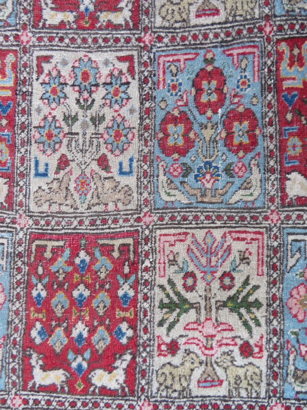 A hand-knotted Persian Qum rug featuring a grid tile pattern filled with floral and animal motifs inside a detailed red border. View VI