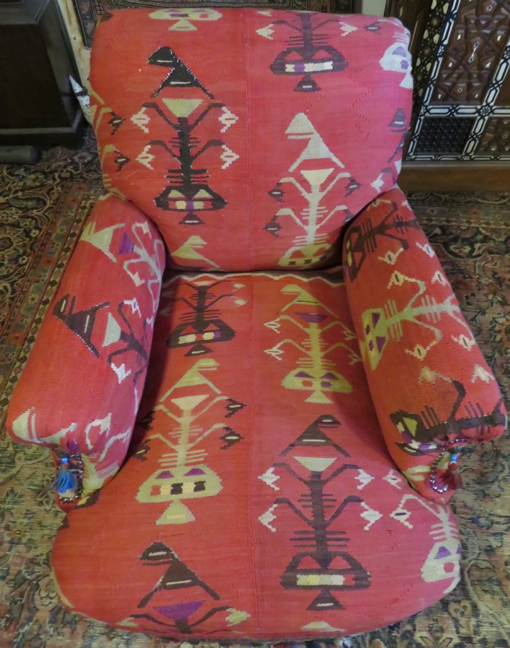 An antique low-slung club armchair upholstered in a geometric red wool kilim textile with turned legs and brass castors. View V