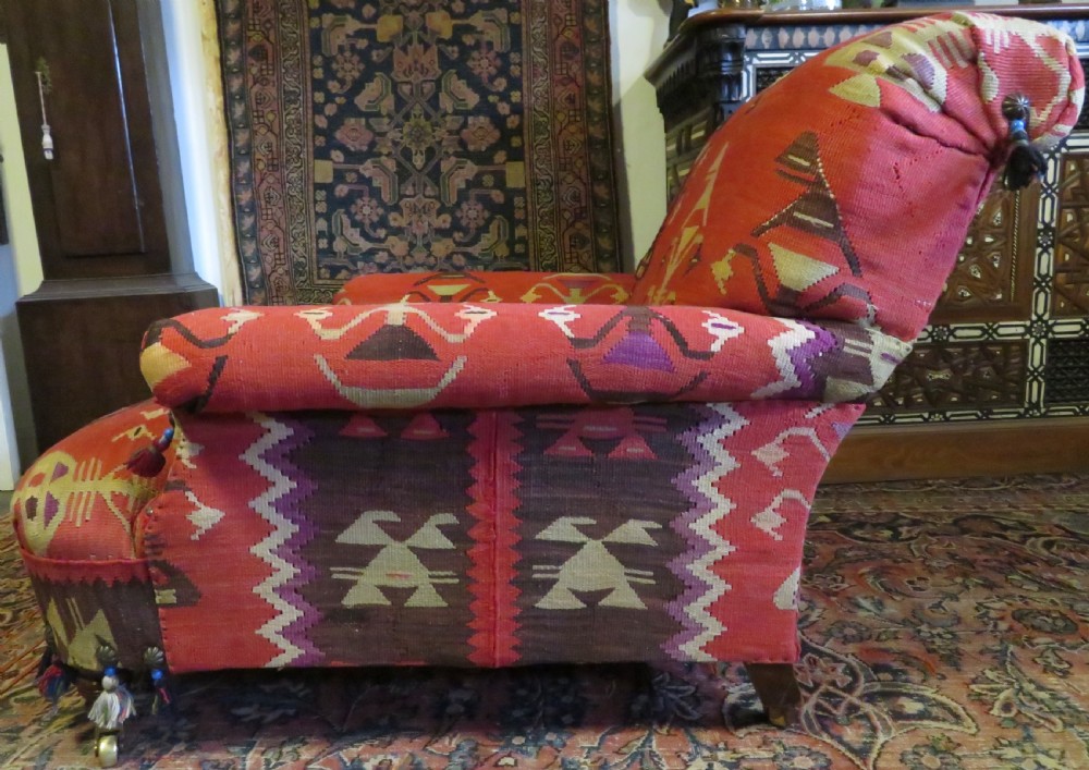 An antique low-slung club armchair upholstered in a geometric red wool kilim textile with turned legs and brass castors. View VI