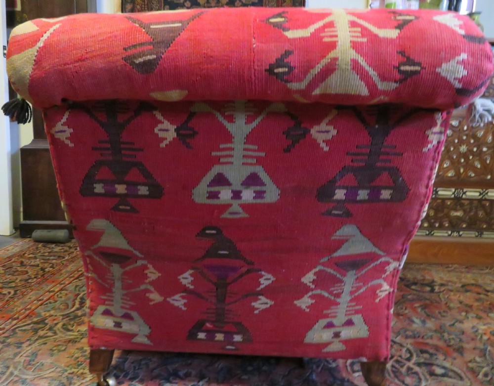 An antique low-slung club armchair upholstered in a geometric red wool kilim textile with turned legs and brass castors. View VII
