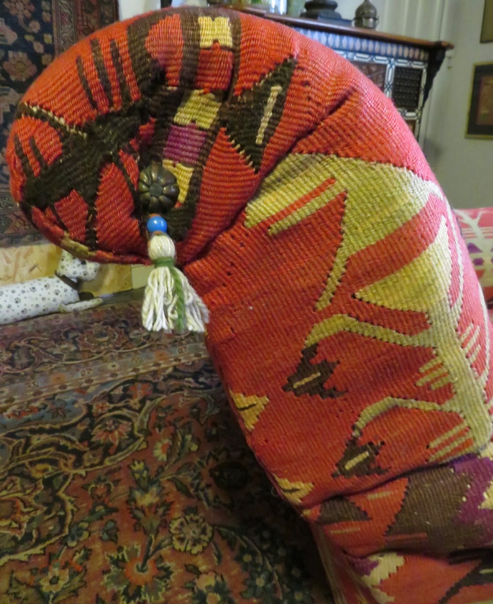An antique low-slung club armchair upholstered in a geometric red wool kilim textile with turned legs and brass castors. View X