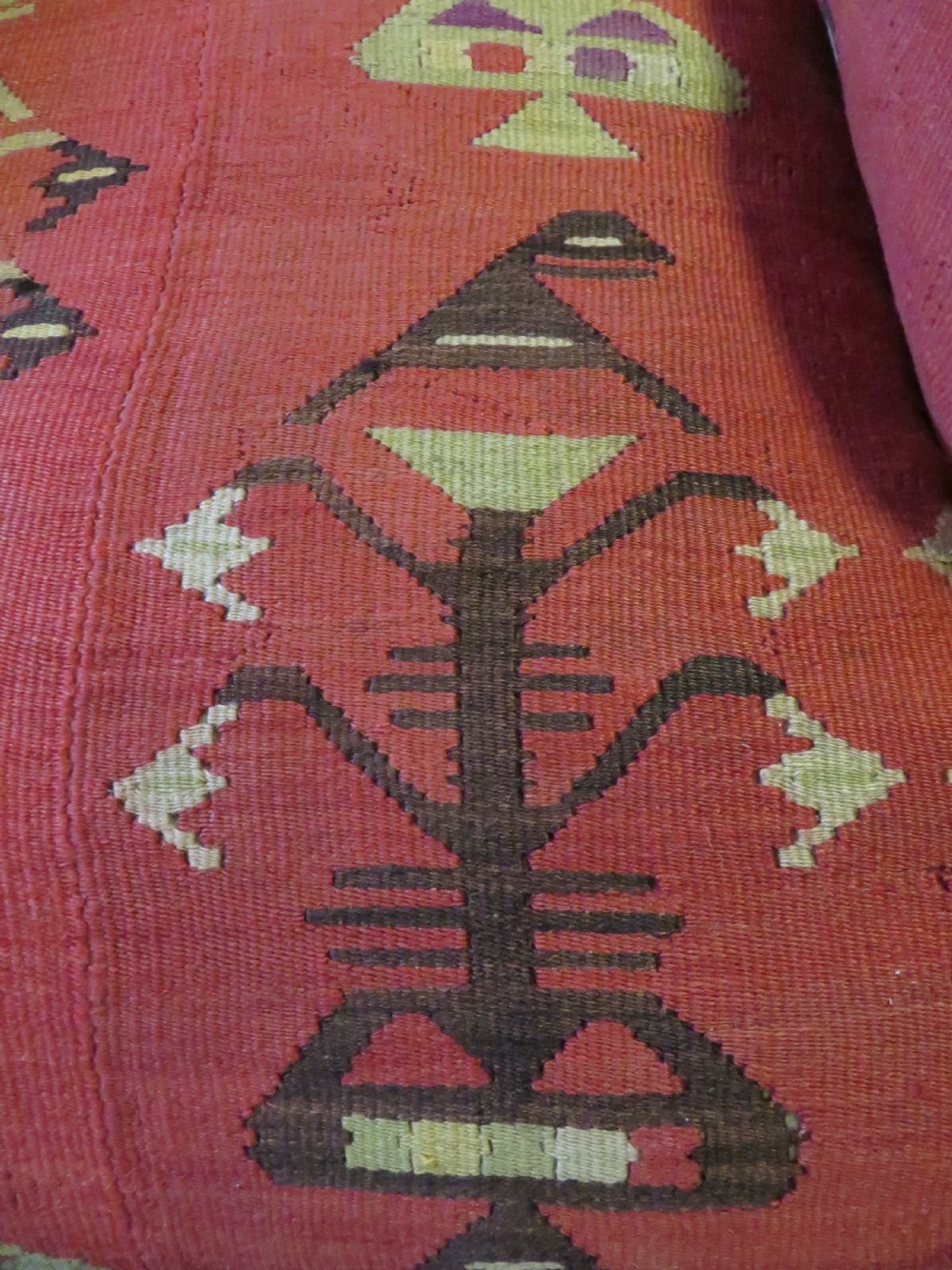 An antique low-slung club armchair upholstered in a geometric red wool kilim textile with turned legs and brass castors. View XII