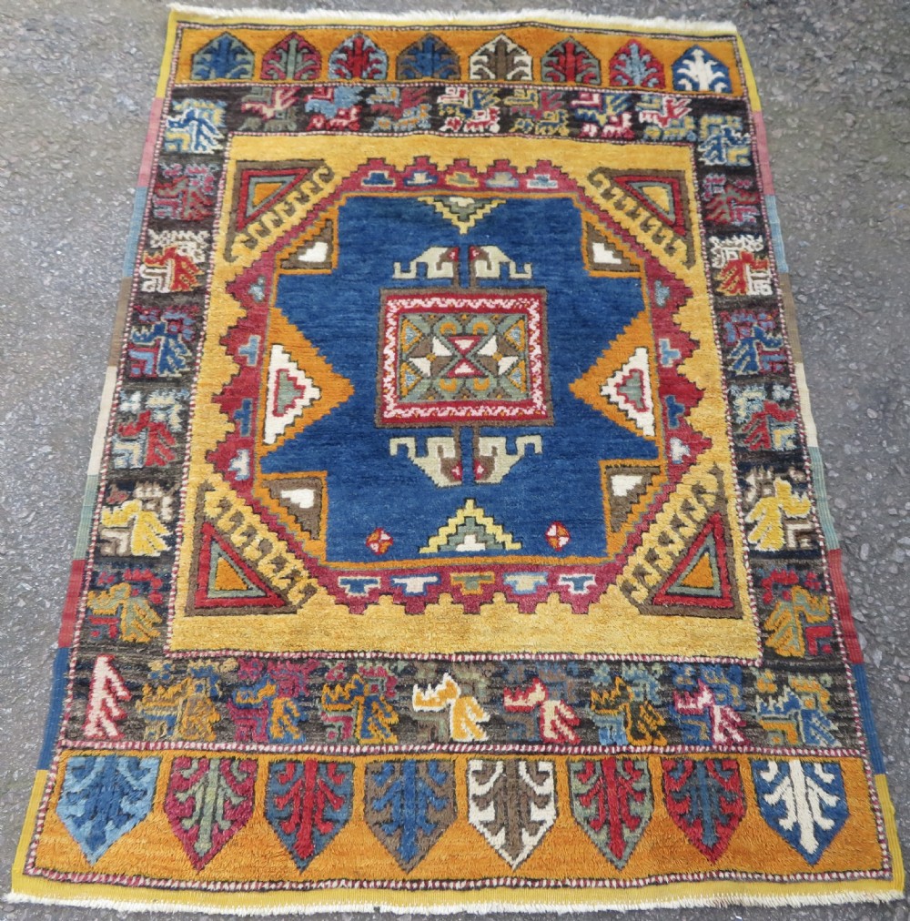 An antique Turkish Konya Yatak wool rug featuring a central indigo blue medallion surrounded by saffron yellow and geometric patterned borders.