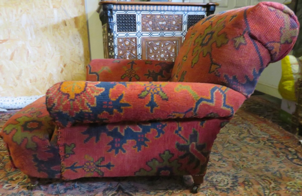 A low-slung, deep-seated Howard and Sons club armchair upholstered in a terracotta red and multi-coloured Ushak carpet pattern with turned legs on brass castors.