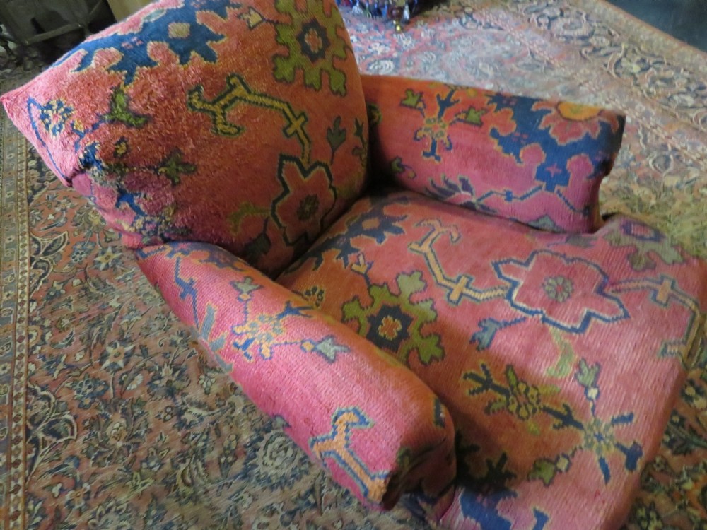 A low-slung, deep-seated Howard and Sons club armchair upholstered in a terracotta red and multi-coloured Ushak carpet pattern with turned legs on brass castors. View VI