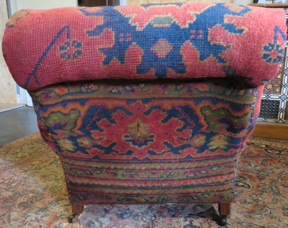 A low-slung, deep-seated Howard and Sons club armchair upholstered in a terracotta red and multi-coloured Ushak carpet pattern with turned legs on brass castors. View VIII