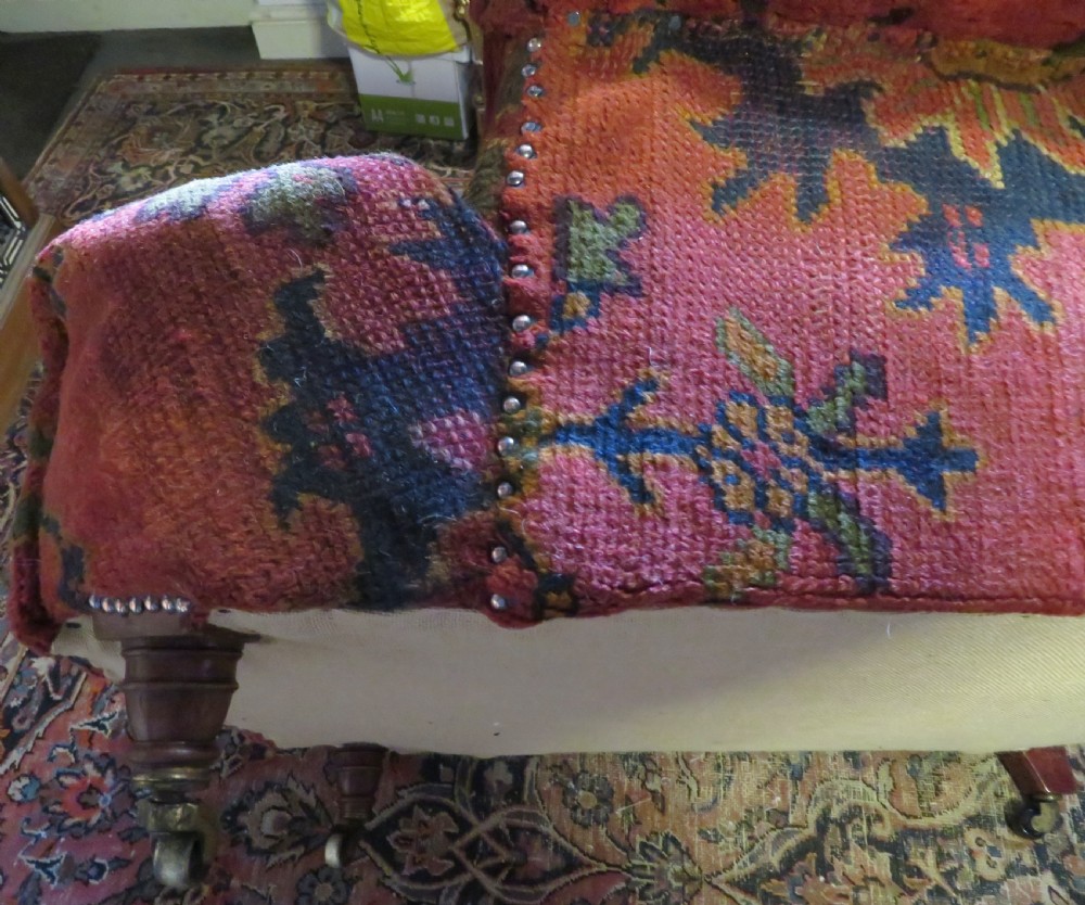 A low-slung, deep-seated Howard and Sons club armchair upholstered in a terracotta red and multi-coloured Ushak carpet pattern with turned legs on brass castors. View XII