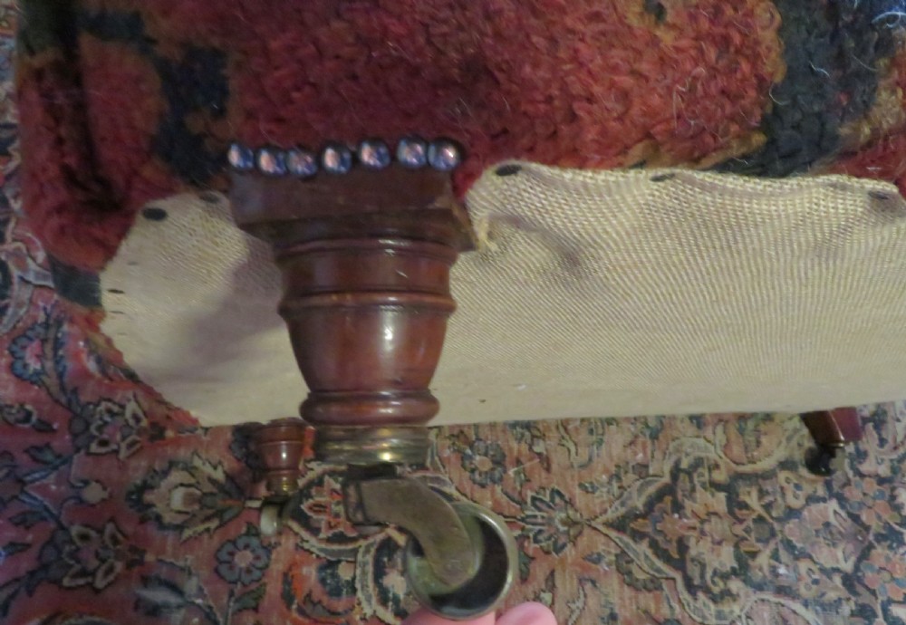 A low-slung, deep-seated Howard and Sons club armchair upholstered in a terracotta red and multi-coloured Ushak carpet pattern with turned legs on brass castors. View XIII