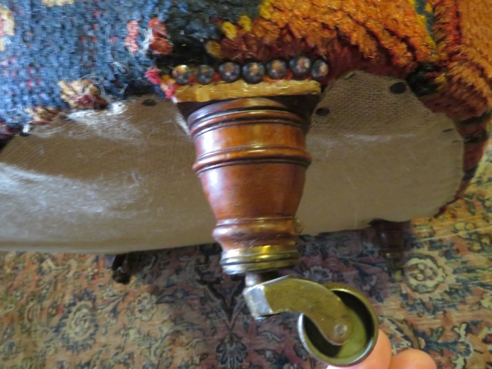 A low-slung, deep-seated Howard and Sons club armchair upholstered in a terracotta red and multi-coloured Ushak carpet pattern with turned legs on brass castors. View XIV