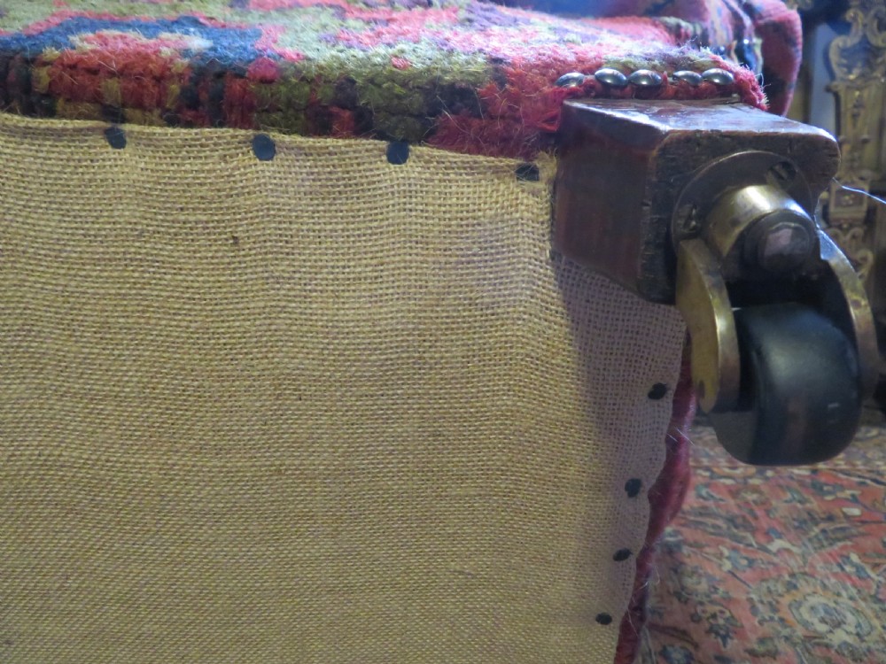 A low-slung, deep-seated Howard and Sons club armchair upholstered in a terracotta red and multi-coloured Ushak carpet pattern with turned legs on brass castors. View XVI