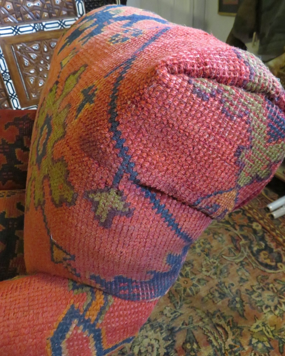 A low-slung, deep-seated Howard and Sons club armchair upholstered in a terracotta red and multi-coloured Ushak carpet pattern with turned legs on brass castors. View XVII