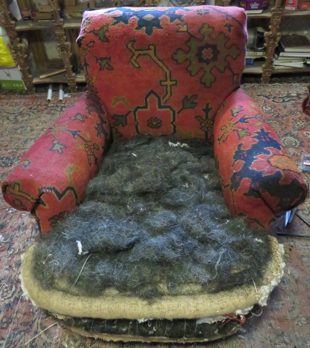 A low-slung, deep-seated Howard and Sons club armchair upholstered in a terracotta red and multi-coloured Ushak carpet pattern with turned legs on brass castors. View XIX