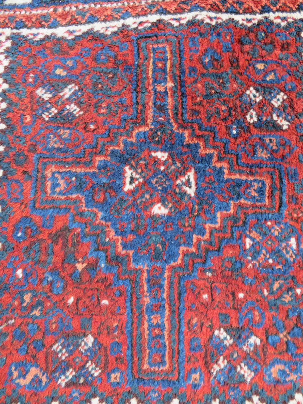 An antique square hand-knotted tribal wool rug panel featuring a central stepped geometric medallion in red, indigo blue, and ivory with fringed edges. View II