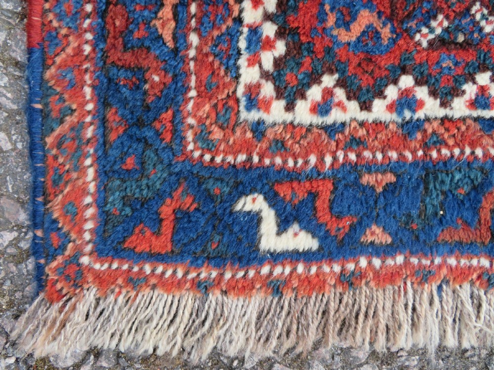 An antique square hand-knotted tribal wool rug panel featuring a central stepped geometric medallion in red, indigo blue, and ivory with fringed edges. View III