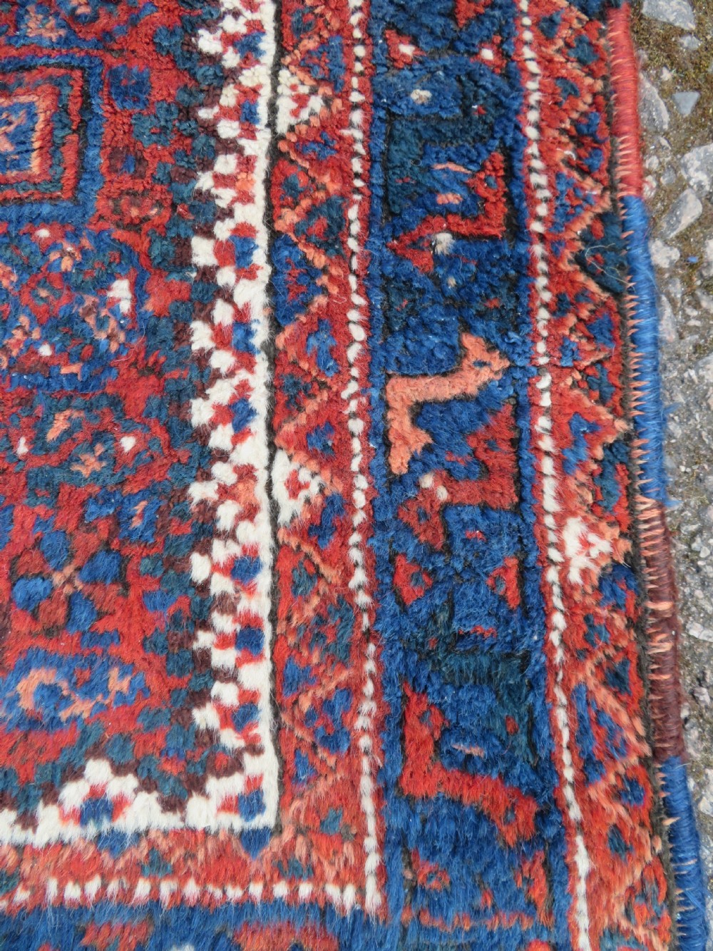 An antique square hand-knotted tribal wool rug panel featuring a central stepped geometric medallion in red, indigo blue, and ivory with fringed edges. View IV