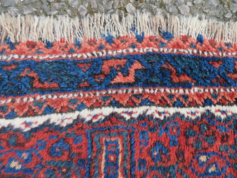 An antique square hand-knotted tribal wool rug panel featuring a central stepped geometric medallion in red, indigo blue, and ivory with fringed edges. View V