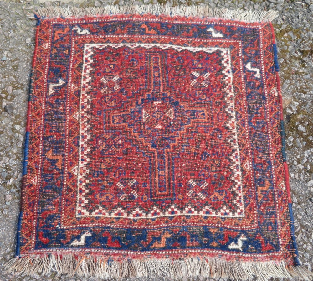 An antique square hand-knotted tribal wool rug panel featuring a central stepped geometric medallion in red, indigo blue, and ivory with fringed edges. View VI