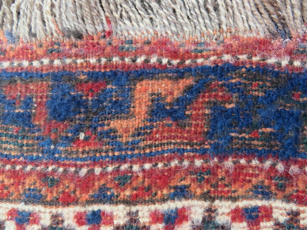 An antique square hand-knotted tribal wool rug panel featuring a central stepped geometric medallion in red, indigo blue, and ivory with fringed edges. View IX