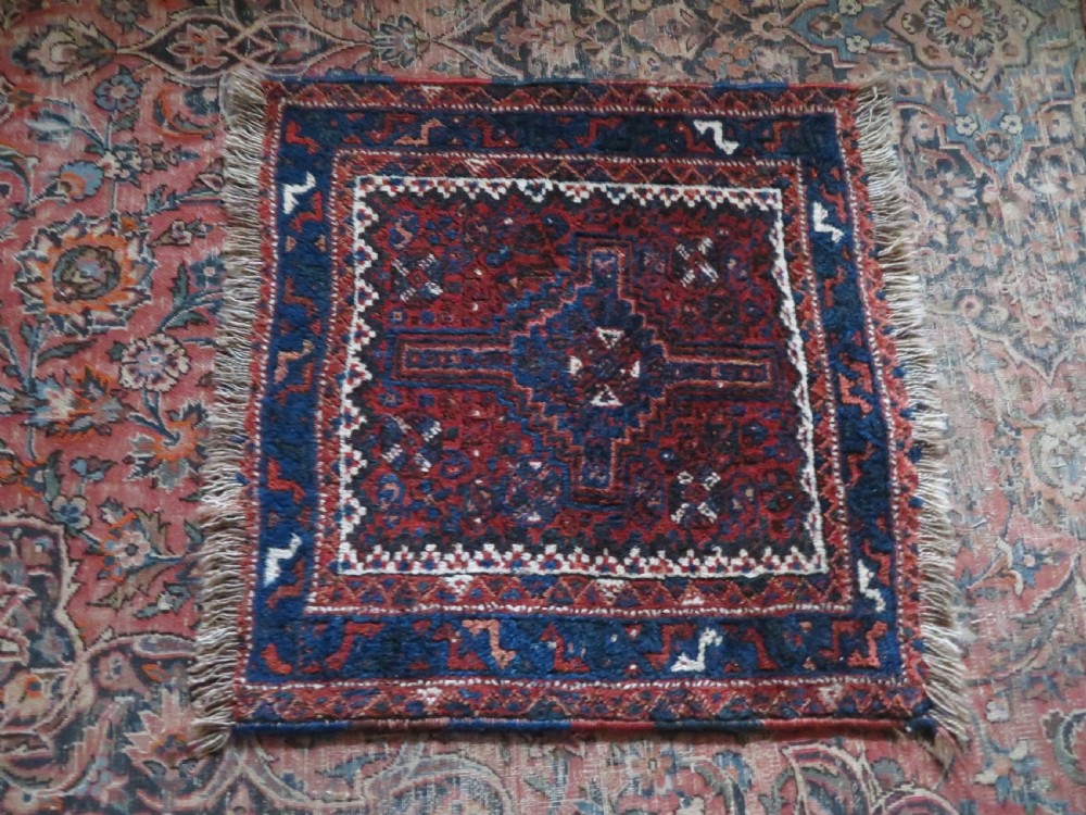 An antique square hand-knotted tribal wool rug panel featuring a central stepped geometric medallion in red, indigo blue, and ivory with fringed edges. View XI