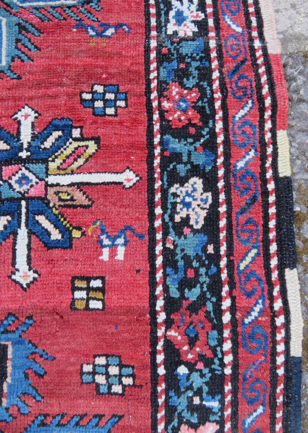 An antique Caucasian Karabagh handwoven wool rug featuring blue and black central geometric medallions on a red field with floral borders. View VII