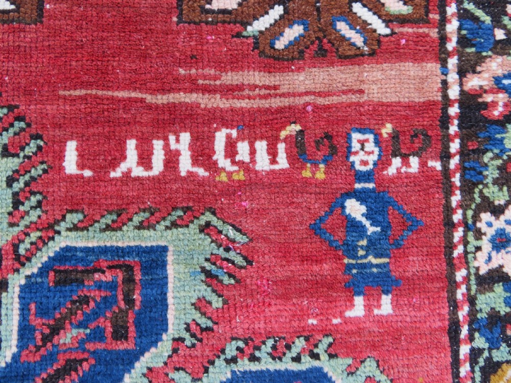 An antique Caucasian Karabagh handwoven wool rug featuring blue and black central geometric medallions on a red field with floral borders. View VIII