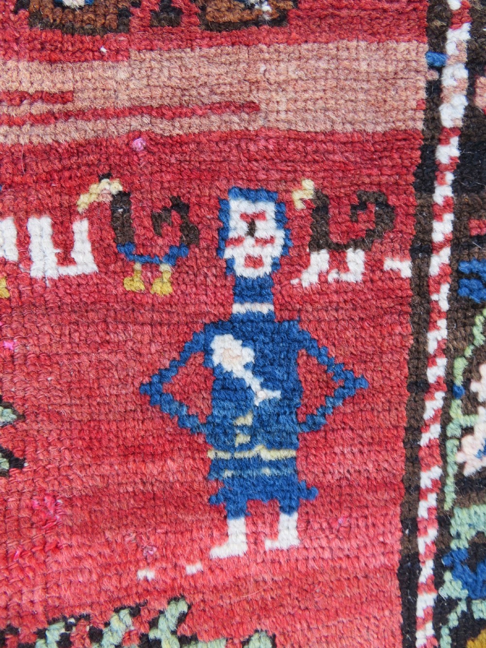 An antique Caucasian Karabagh handwoven wool rug featuring blue and black central geometric medallions on a red field with floral borders. View IX
