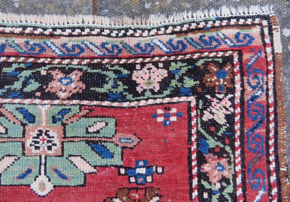 An antique Caucasian Karabagh handwoven wool rug featuring blue and black central geometric medallions on a red field with floral borders. View XI