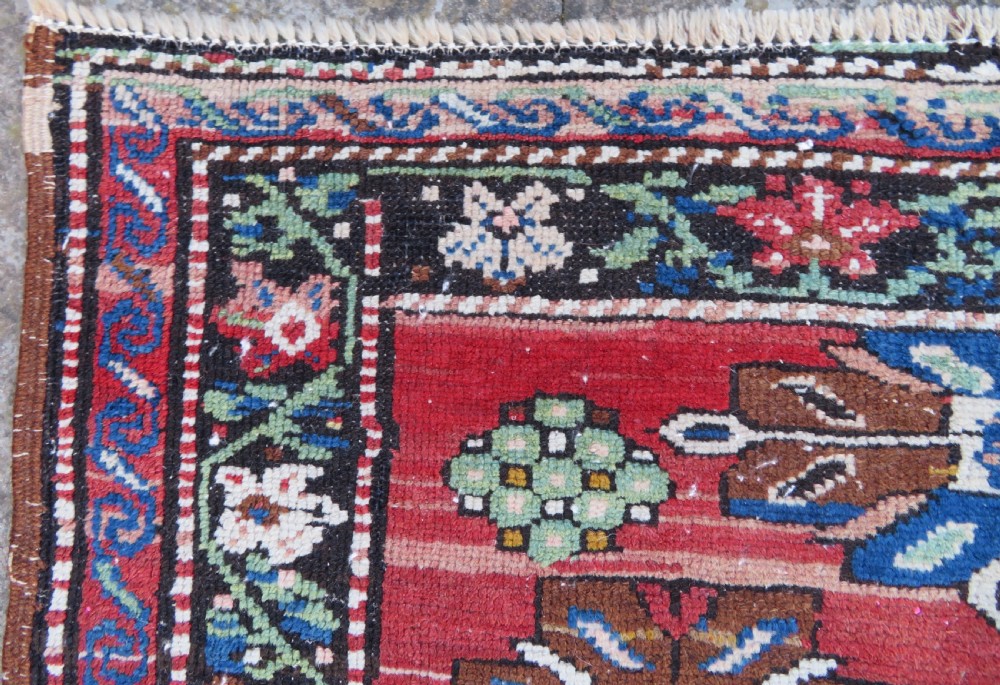 An antique Caucasian Karabagh handwoven wool rug featuring blue and black central geometric medallions on a red field with floral borders. View XII