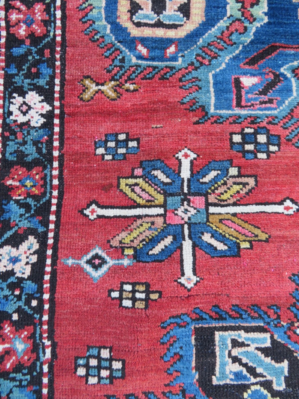 An antique Caucasian Karabagh handwoven wool rug featuring blue and black central geometric medallions on a red field with floral borders. View XIII