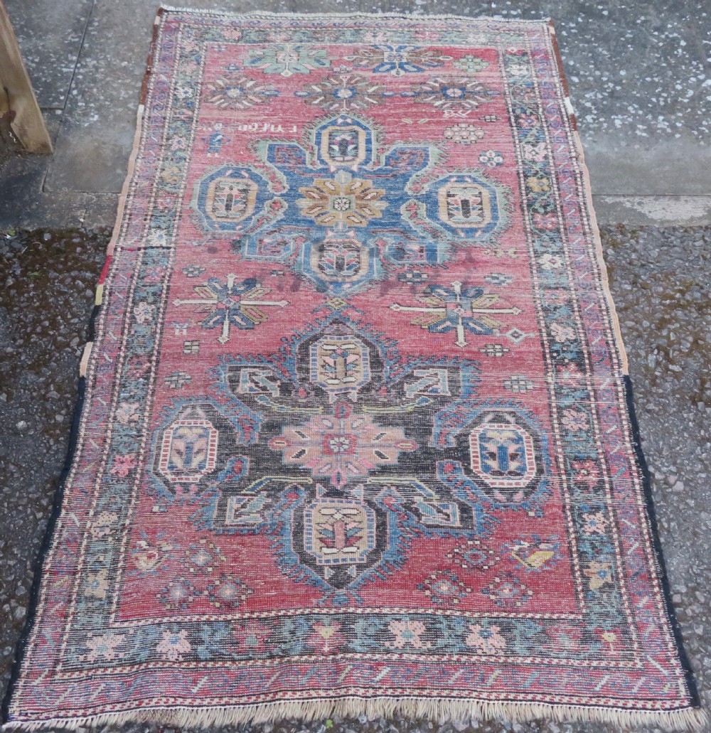 An antique Caucasian Karabagh handwoven wool rug featuring blue and black central geometric medallions on a red field with floral borders. View XV