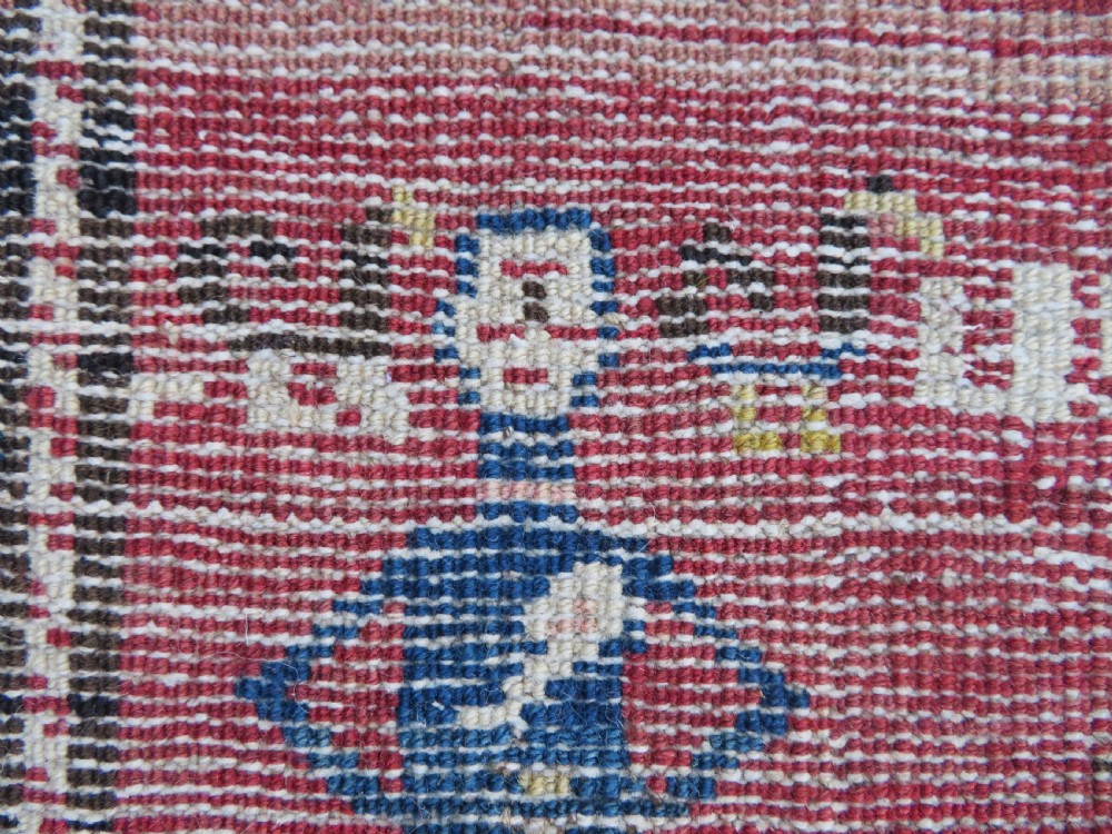 An antique Caucasian Karabagh handwoven wool rug featuring blue and black central geometric medallions on a red field with floral borders. View XVI