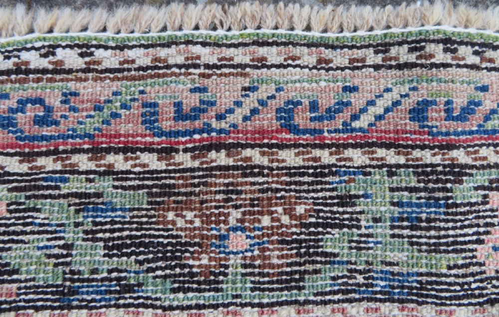 An antique Caucasian Karabagh handwoven wool rug featuring blue and black central geometric medallions on a red field with floral borders. View XVII