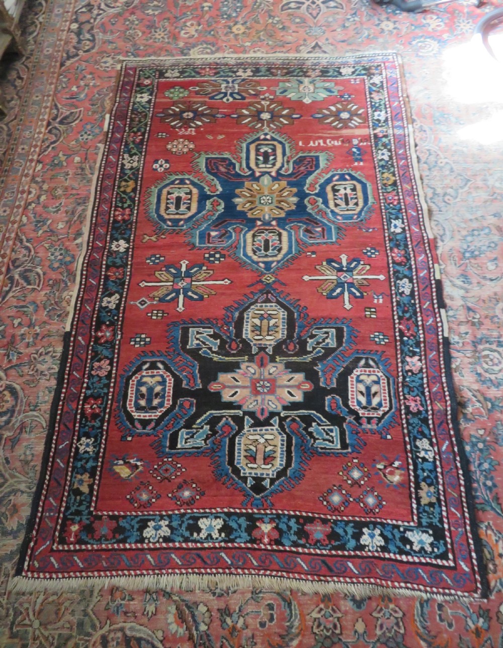 An antique Caucasian Karabagh handwoven wool rug featuring blue and black central geometric medallions on a red field with floral borders. View XX
