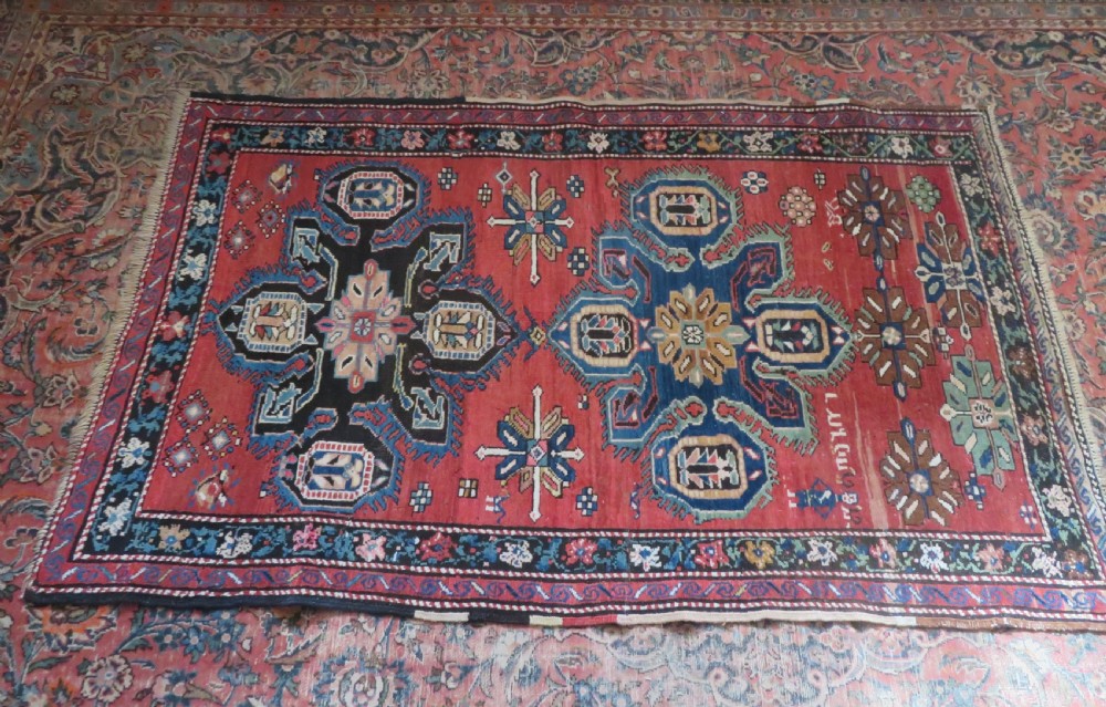 An antique Caucasian Karabagh handwoven wool rug featuring blue and black central geometric medallions on a red field with floral borders. View XXI