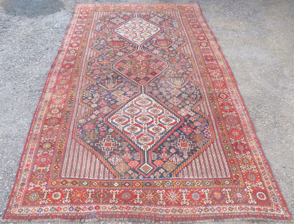 An antique hand-knotted Khamseh tribal carpet featuring multiple diamond medallions and geometric borders in navy blue, terracotta red, and cream wool.