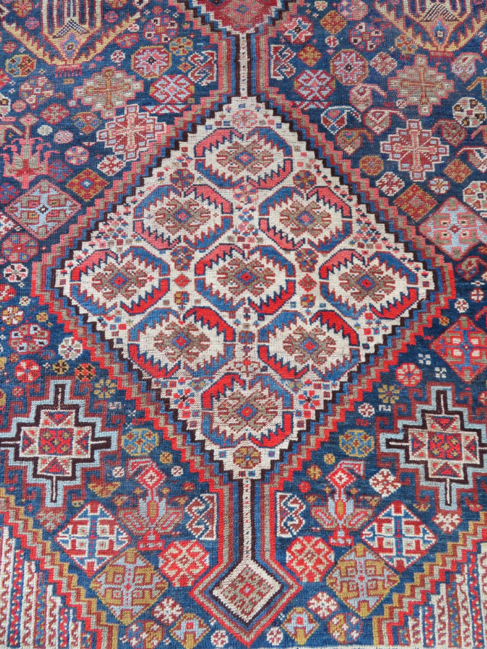 An antique hand-knotted Khamseh tribal carpet featuring multiple diamond medallions and geometric borders in navy blue, terracotta red, and cream wool. View IV
