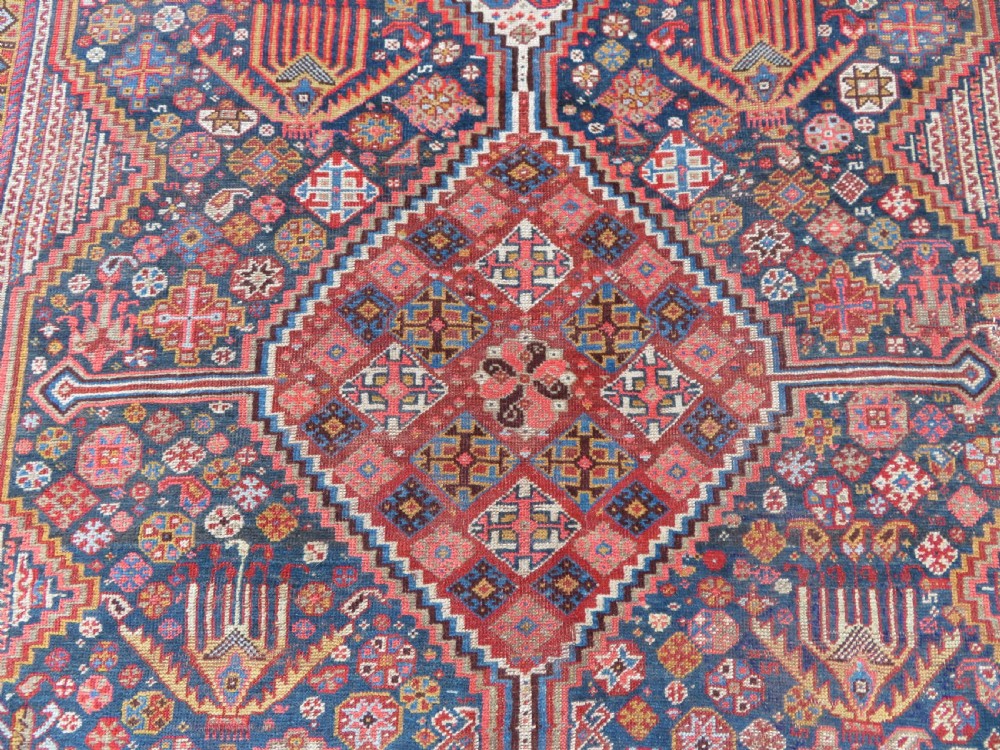 An antique hand-knotted Khamseh tribal carpet featuring multiple diamond medallions and geometric borders in navy blue, terracotta red, and cream wool. View V
